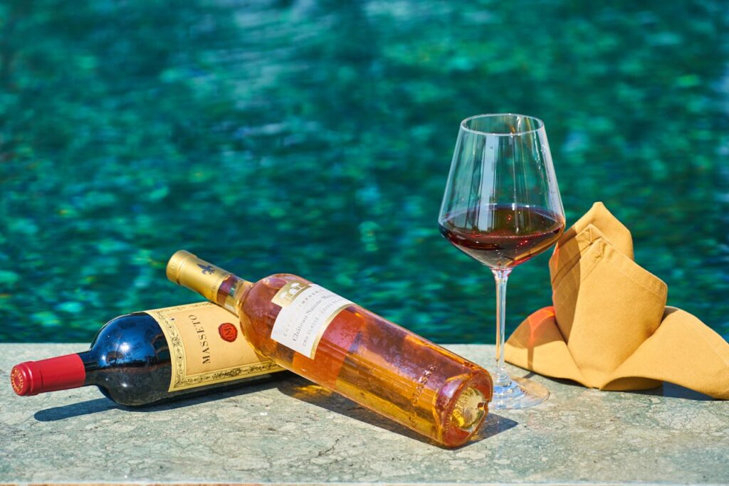 Two Labeled  Bottles Of Wine Beside A Wine Glass By The Pool